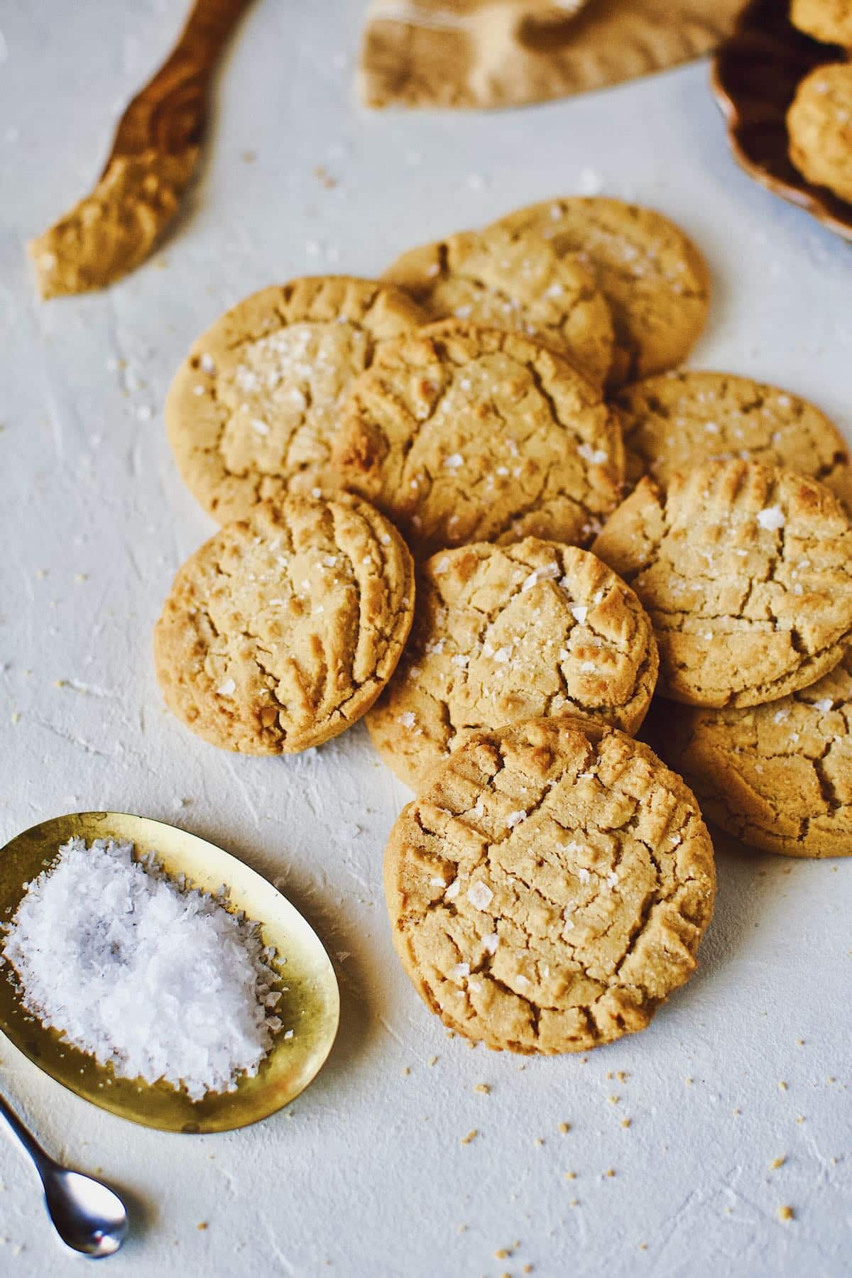 Cookies piled up on a counter sprinkled with flakey sea salt.