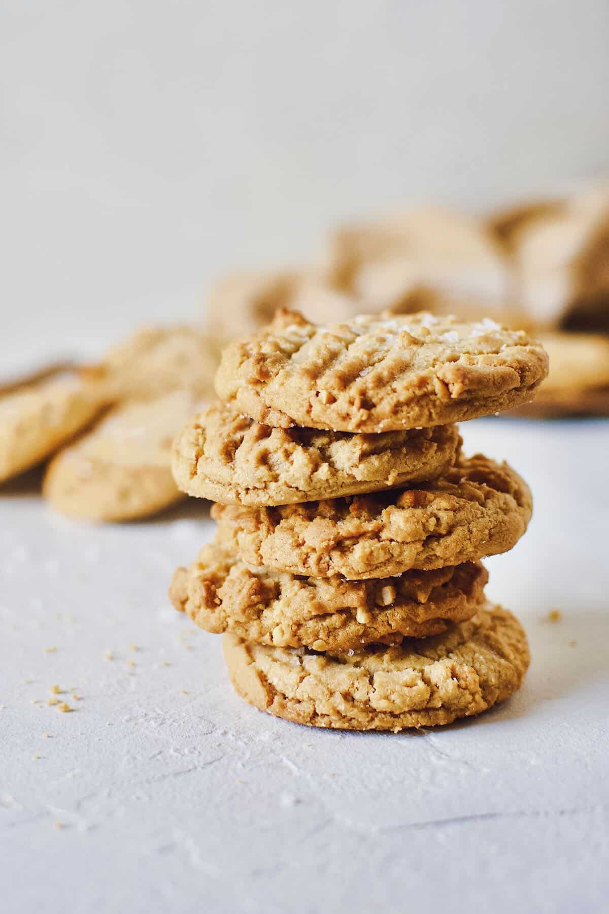 Cookies stacked up on a counter sprinkled with flakey sea salt.