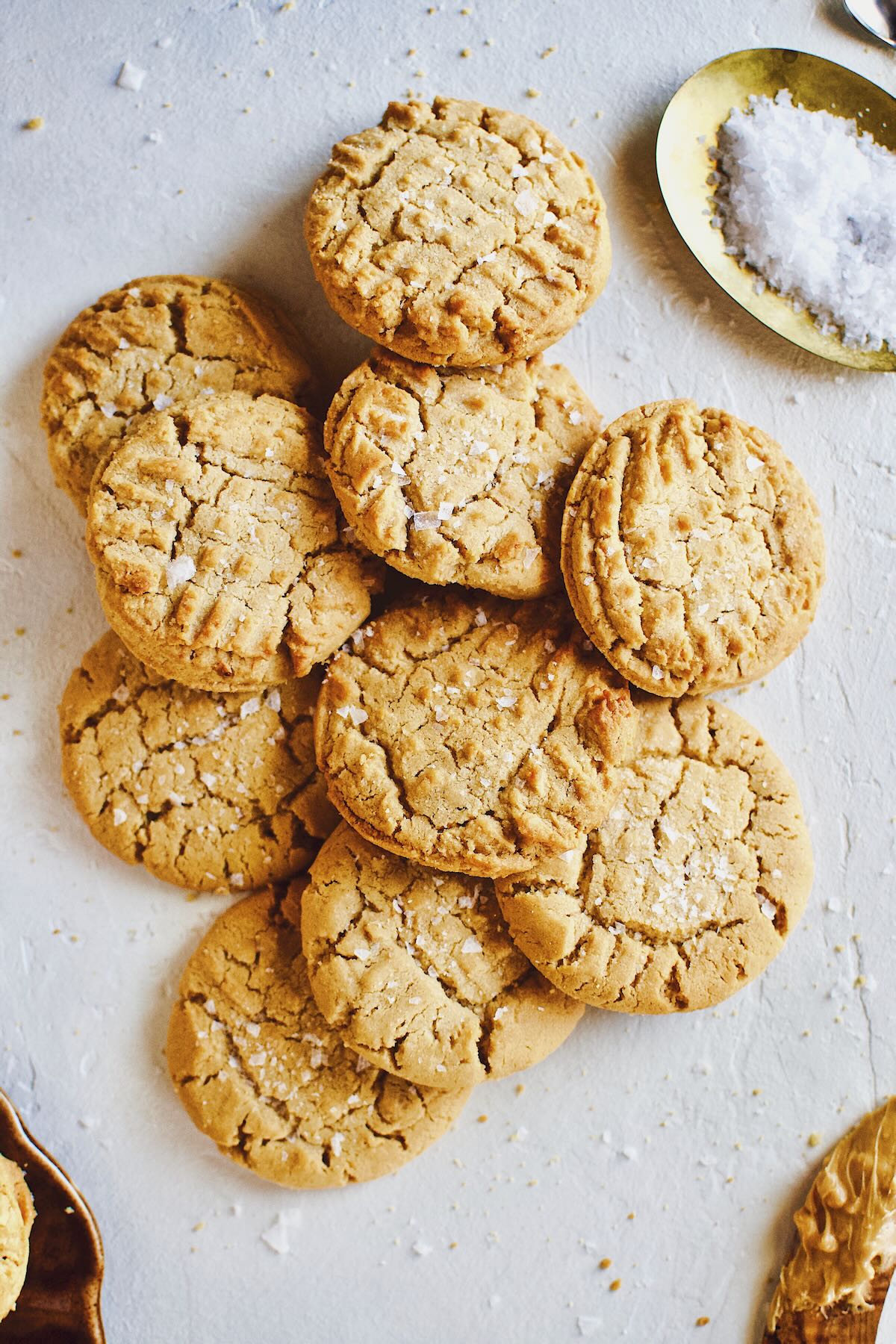 Cookies piled up on a counter sprinkled with flakey sea salt.