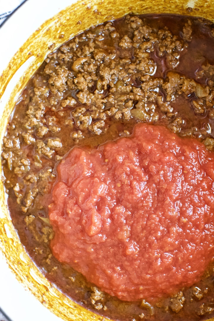 Adding crushed tomatoes to the pot to finish the chili.