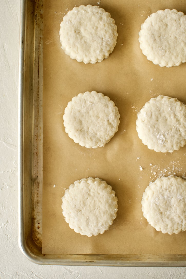 Scones cut with a fluted cutter and lined up on a parchment-lined baking tray.
