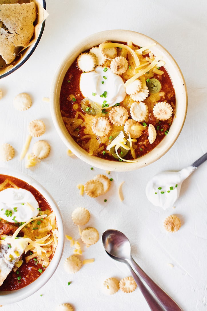 Spicy Texas Chili in two bowls surrounded by various toppings.