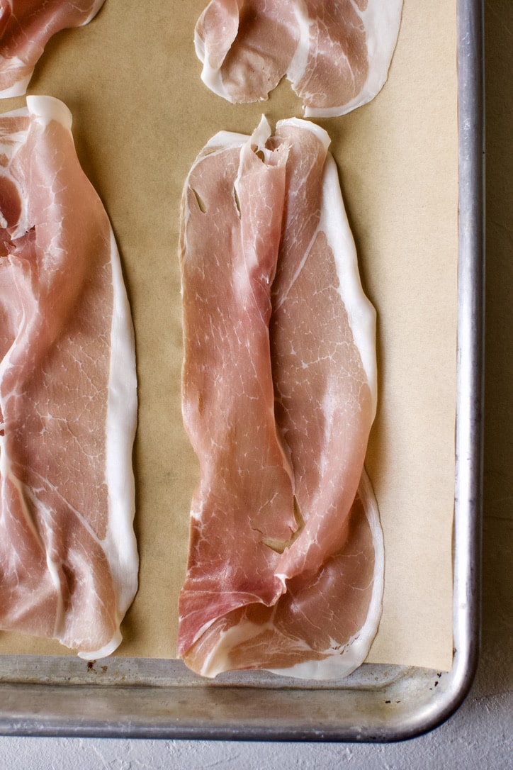 Prosciutto laid out on a parchment-lined baking sheet.