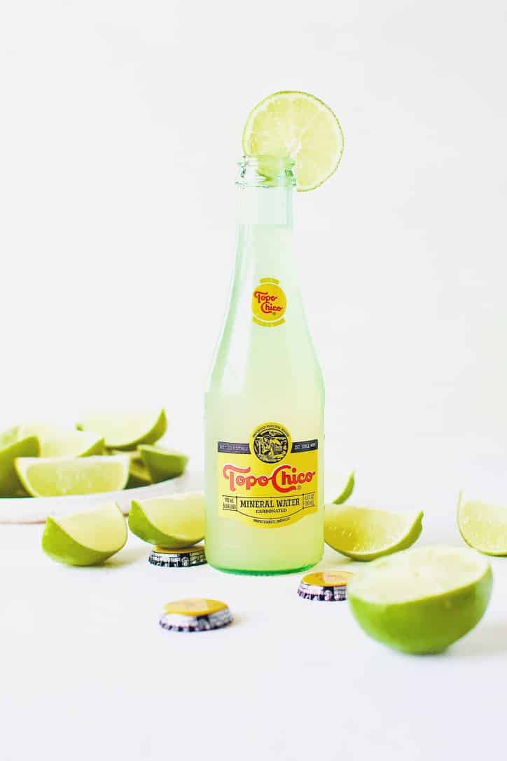 Topo Chico Margaritas bottled cocktails, surrounded by wedged limes.