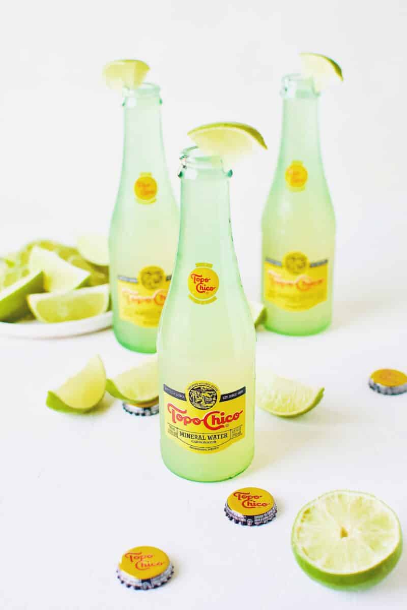 Topo Chico Margaritas bottled cocktails, surrounded by wedged limes.