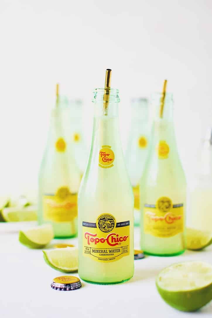 Topo Chico Margaritas bottled cocktails, surrounded by wedged limes.