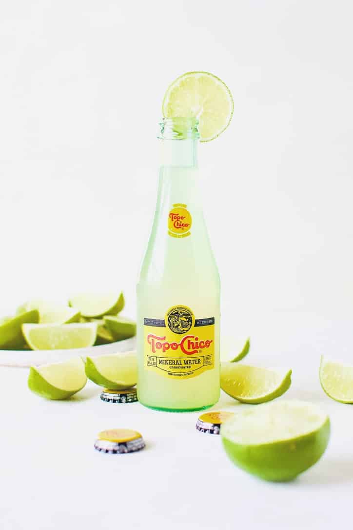 Topo Chico Margaritas bottled cocktails, surrounded by wedged limes.