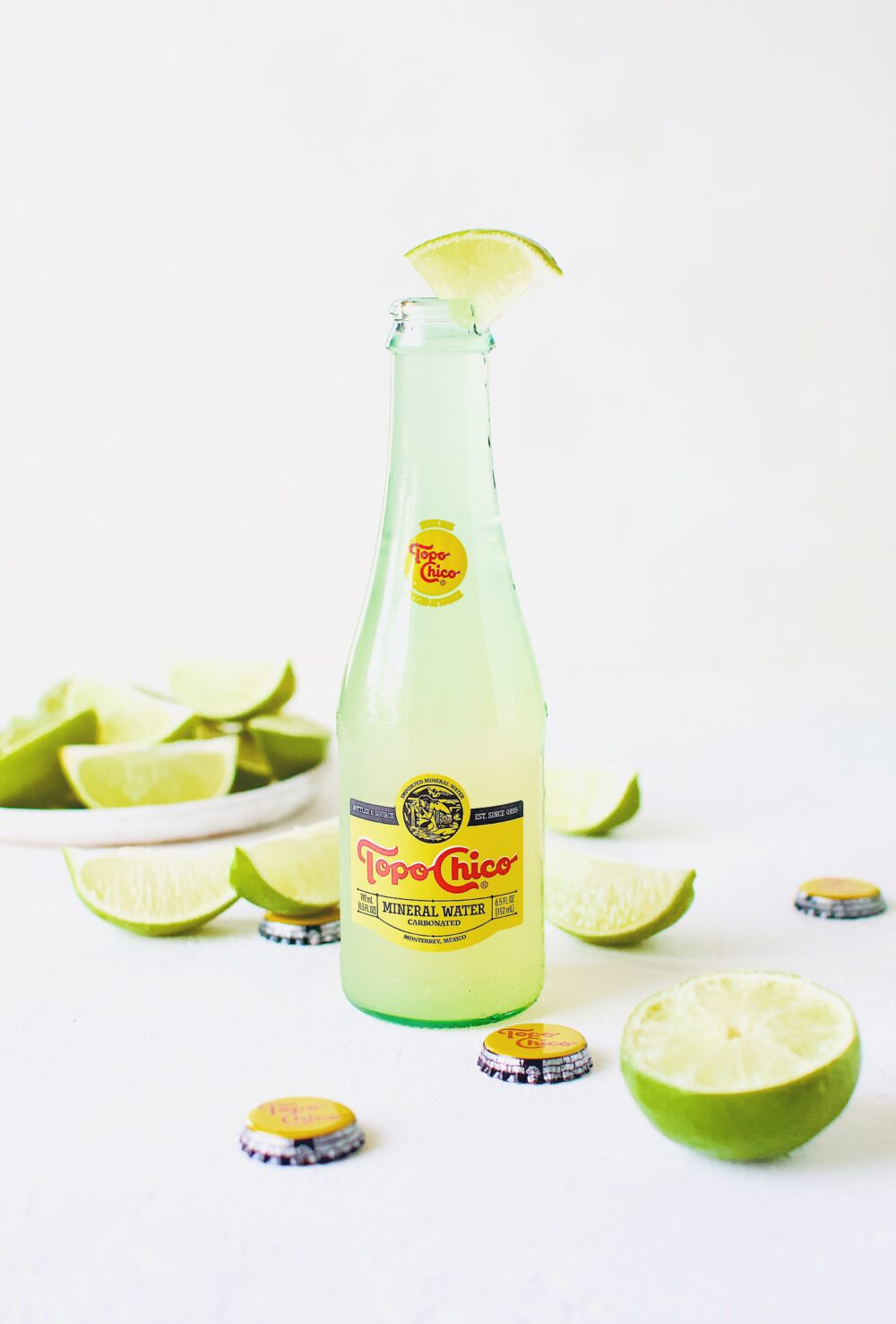 Topo Chico Margarita served in the bottle, surrounded by wedged limes.