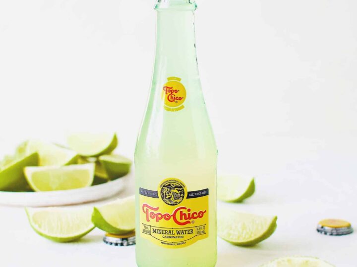 Topo Chico Margarita served in the bottle, surrounded by wedged limes.