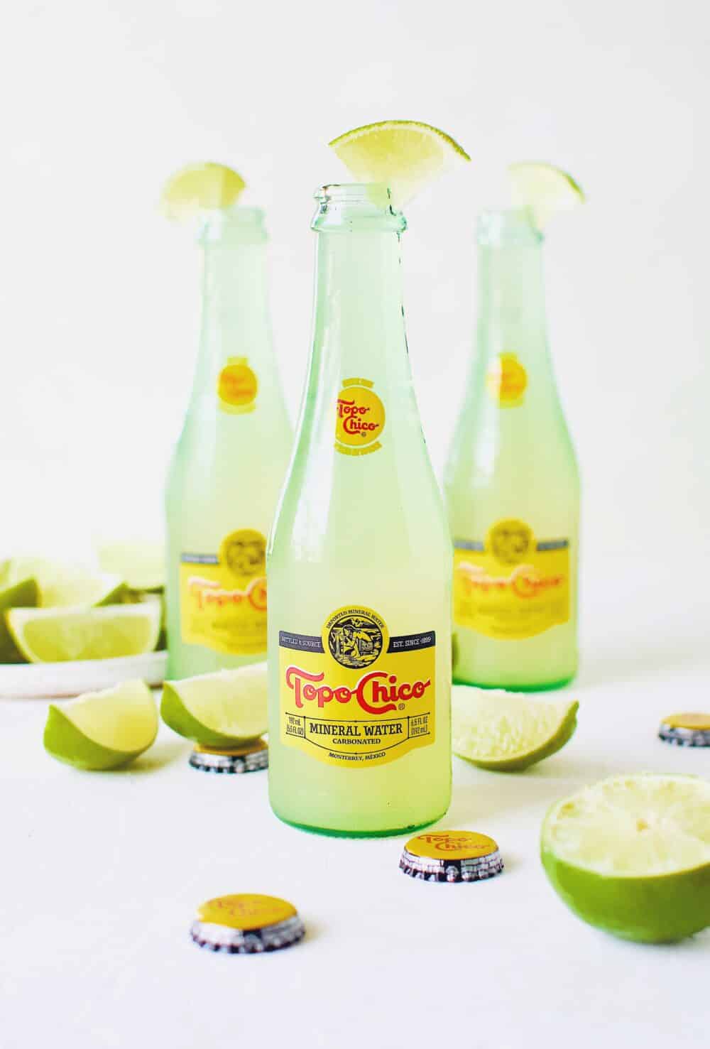 Topo Chico Margaritas bottled cocktails, surrounded by wedged limes.