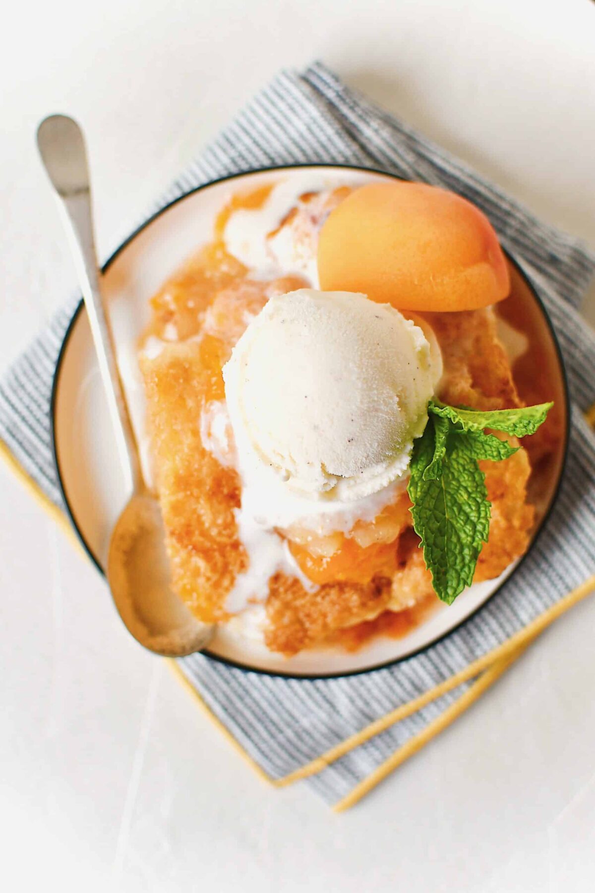 Apricot Cobbler served on small plates with a scoop of vanilla ice cream on top, a slice of fresh apricot, a sprig of mint, and a spoon to eat it with.