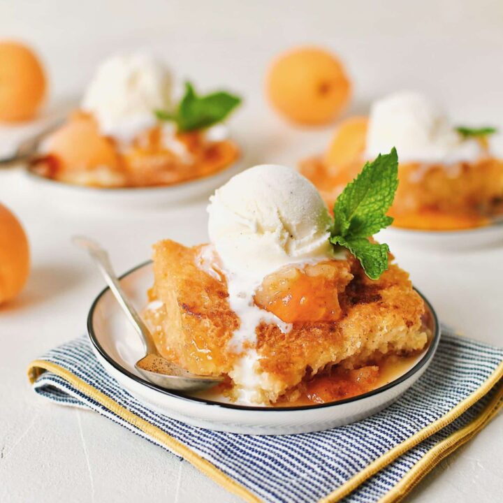 Apricot Cobbler served on small plates with a scoop of vanilla ice cream on top, a slice of fresh apricot, a sprig of mint, and a spoon to eat it with.