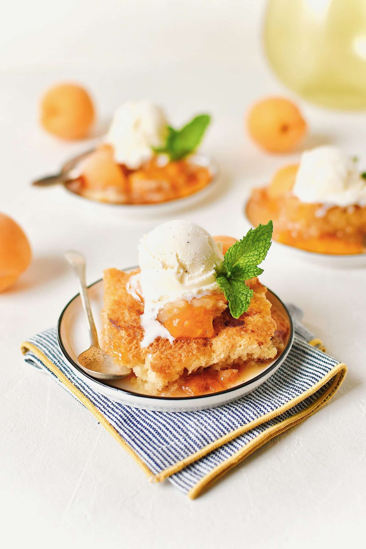 Apricot Cobbler served on small plates with a scoop of vanilla ice cream on top, a slice of fresh apricot, a sprig of mint, and a spoon to eat it with.