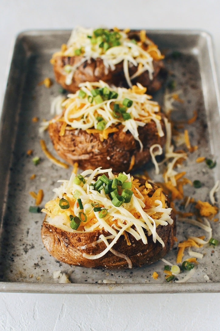 Crispy Skin Baked Potatoes topped with white and sharp cheddar cheeses and green onions.