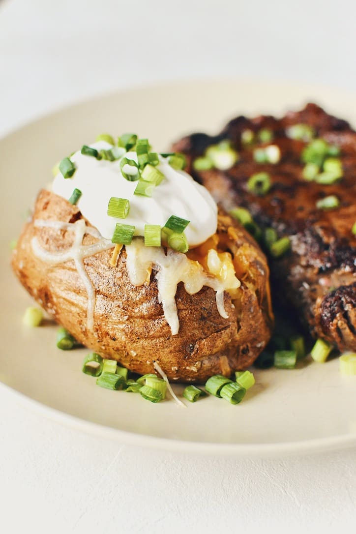 Crispy Skin Baked Potatoes topped with white and sharp cheddar cheeses, sour cream, and green onions.