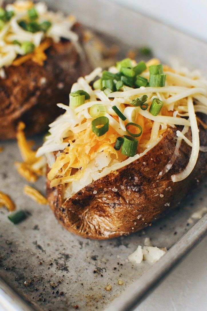 Crispy Skin Baked Potatoes topped with white and sharp cheddar cheeses and green onions.