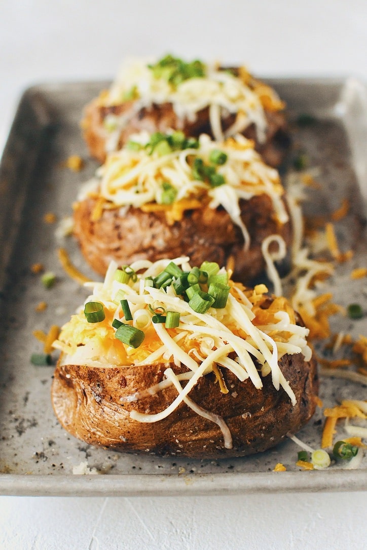 Crispy Skin Baked Potatoes topped with white and sharp cheddar cheeses and green onions.