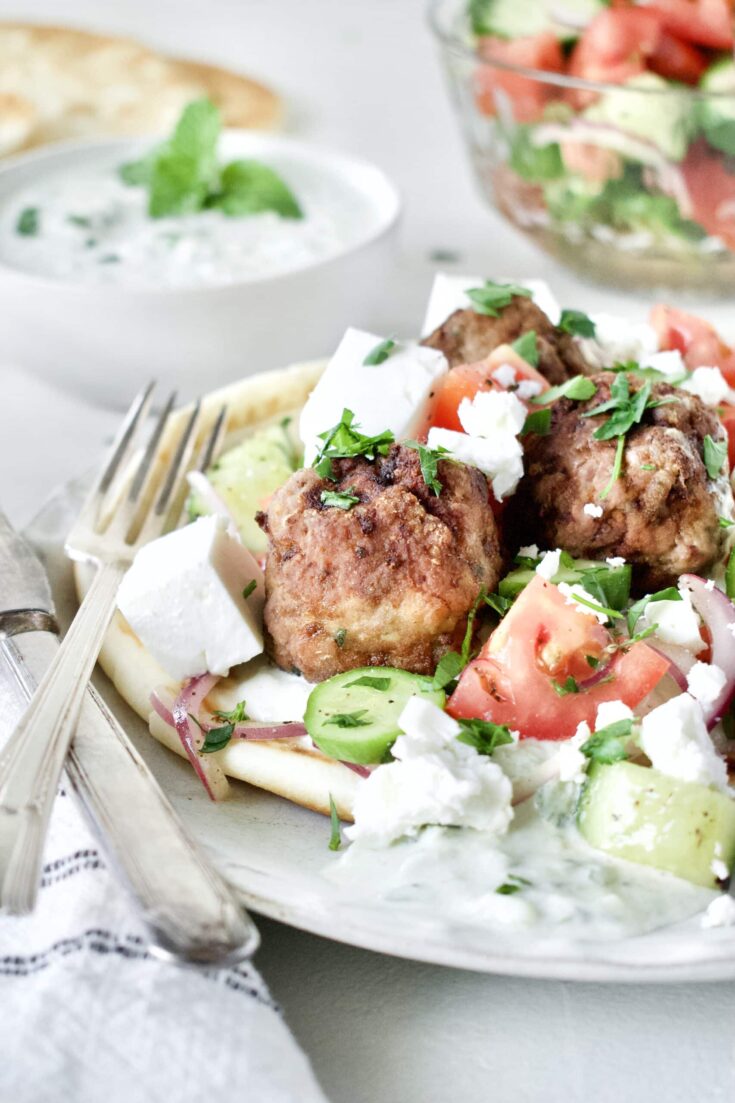 Greek Meatballs served with Greek Salad on top, over a pita bread with Tzatziki sauce.