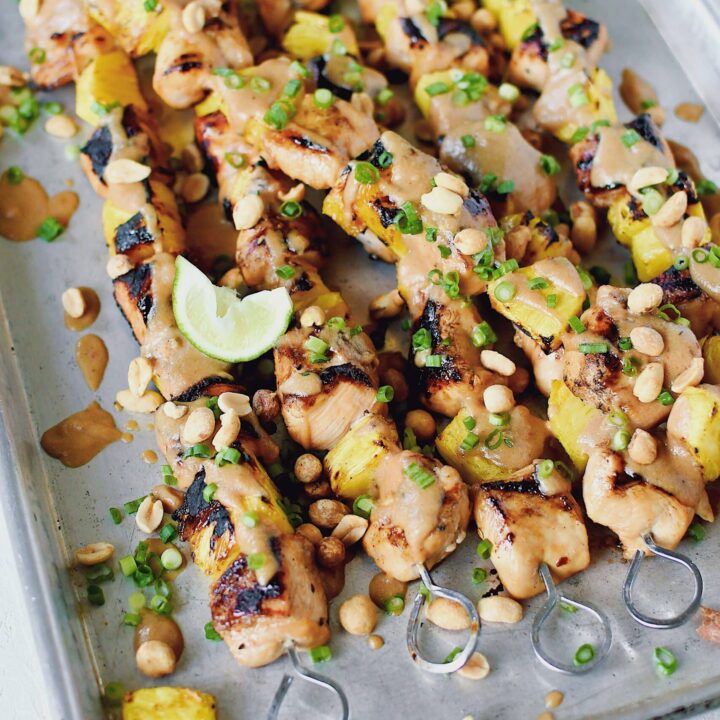 Pineapple Peanut Chicken Skewers fresh off the grill topped with peanut sauce, chopped green onions, and chopped peanuts.
