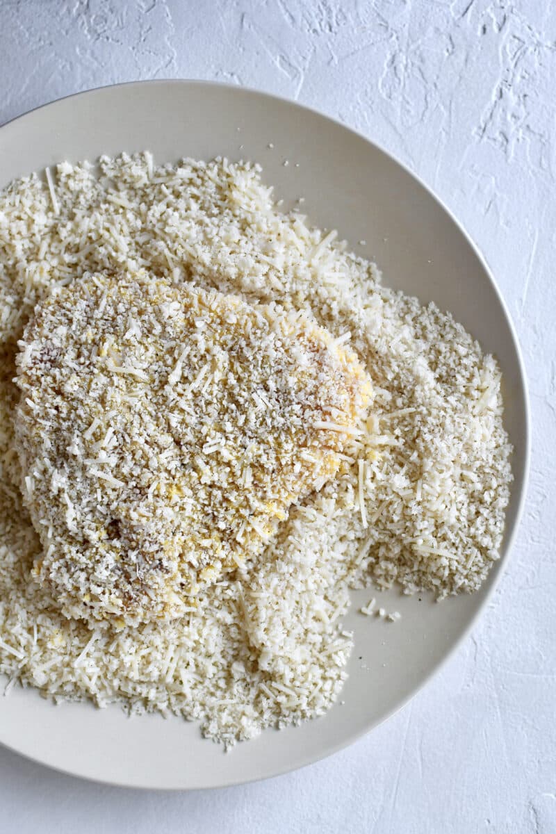 Chicken Breast Split in half, after tenderizing, seasoning with salt and pepper, dusting with flour, dredged in eggs, and now being crusted in parmesan and bread crumbs.