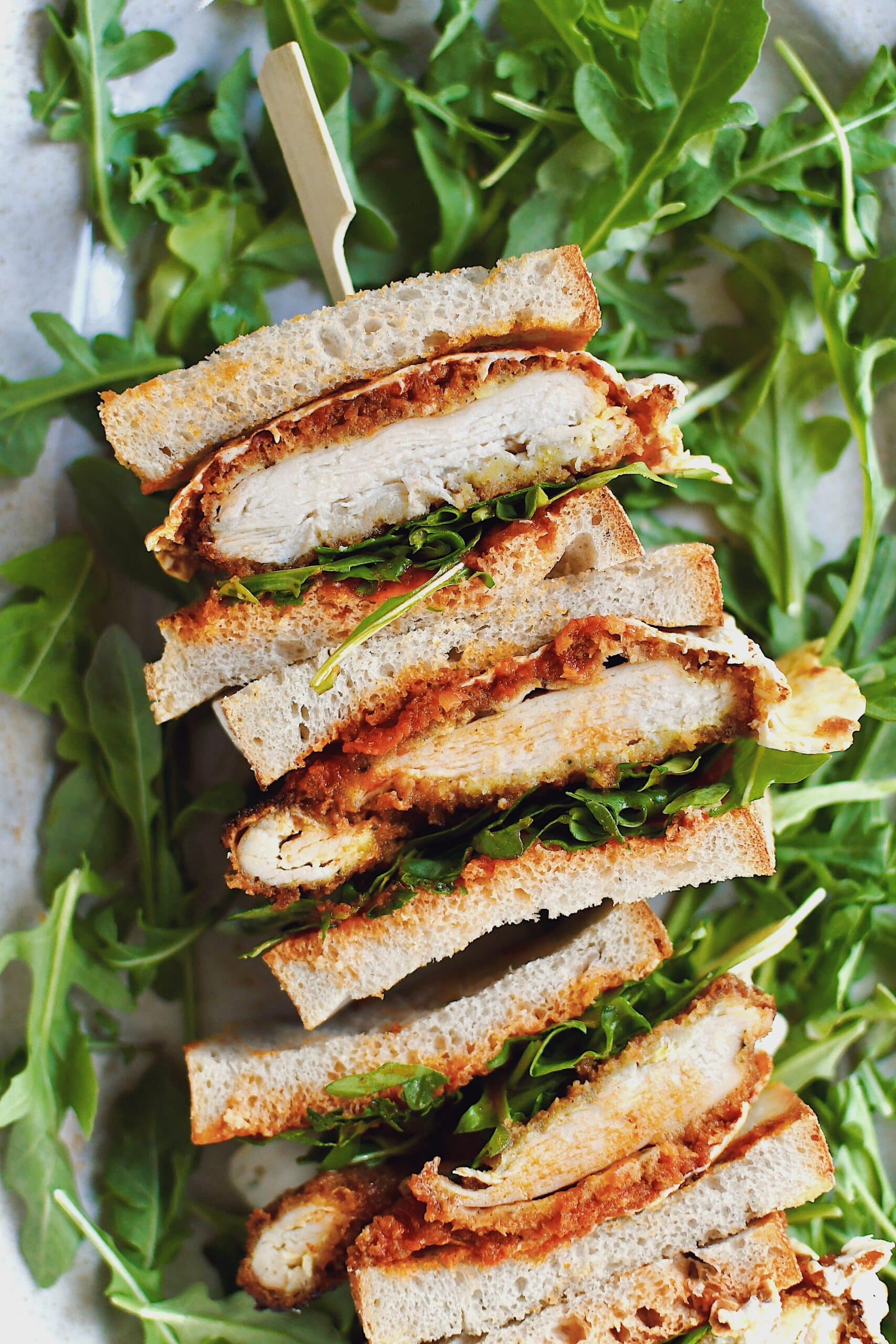 Parmesan Chicken Sandwich, sliced and stacked, laid on a platter on a bed of arugula.