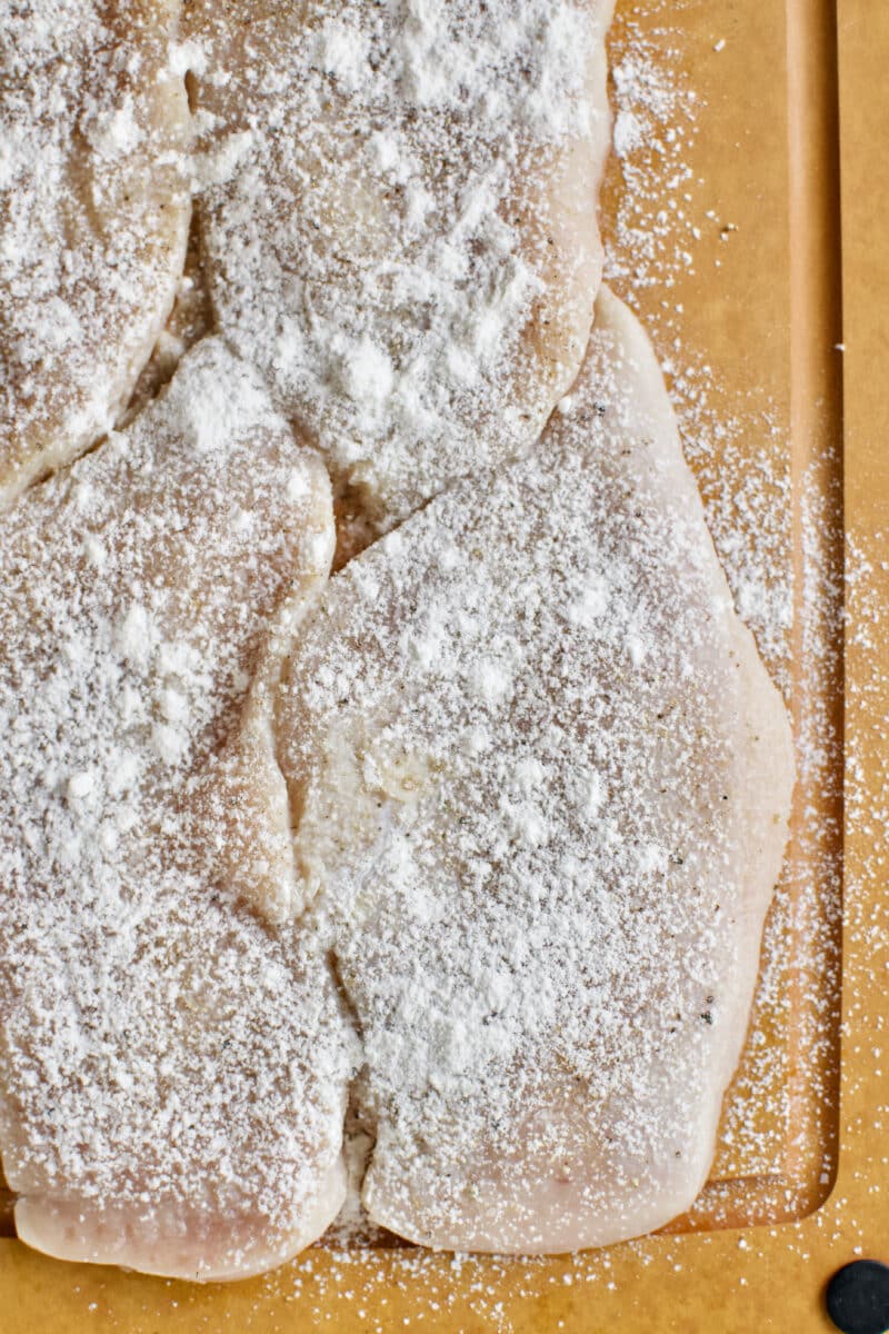 Seasoning split and tenderized chicken breasts with salt, pepper, garlic powder, and dusted with flour.