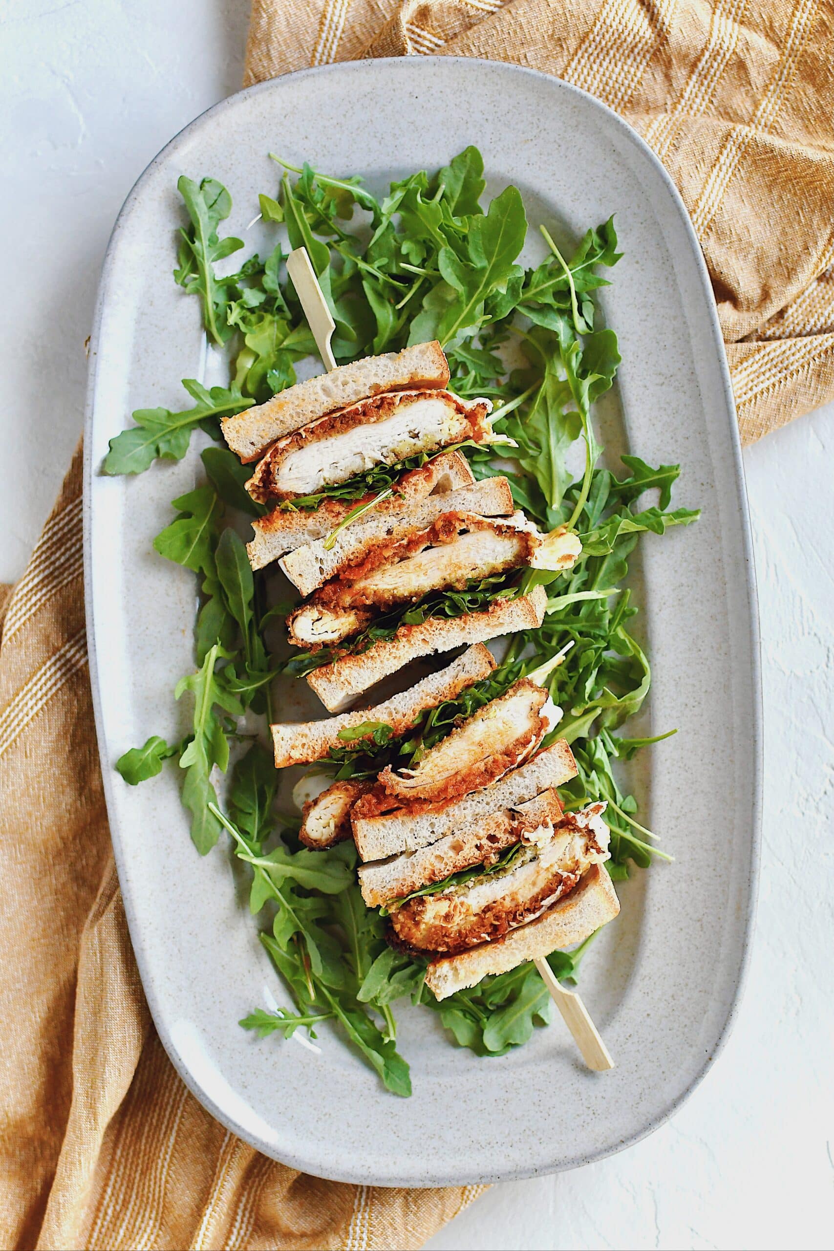 Parmesan Chicken Sandwich, sliced and stacked, laid on a platter on a bed of arugula.