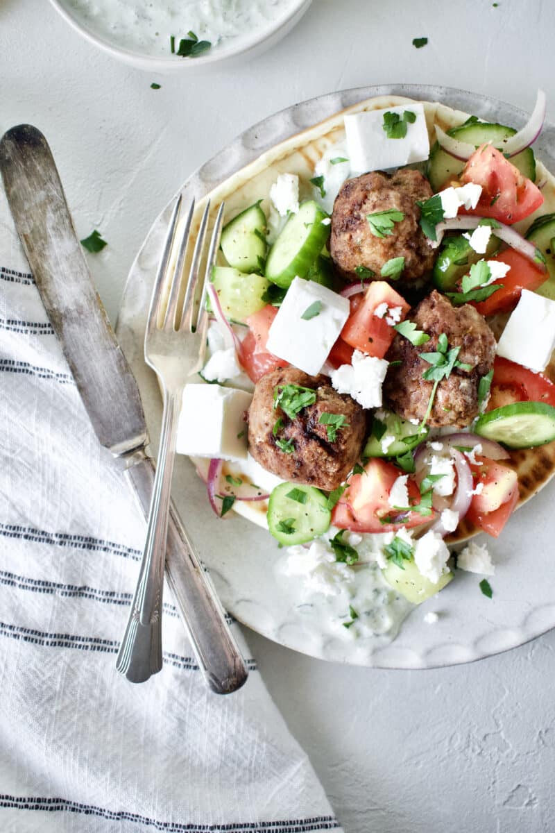 Greek Meatballs served with Greek Salad on top, over a pita bread with Tzatziki sauce.