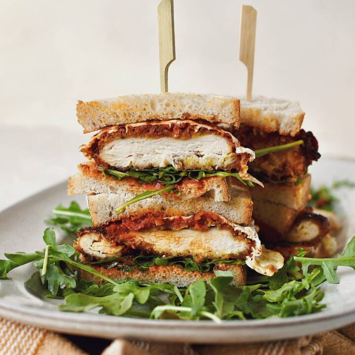 Parmesan Chicken Sandwich, sliced and stacked, on a platter on a bed of arugula.