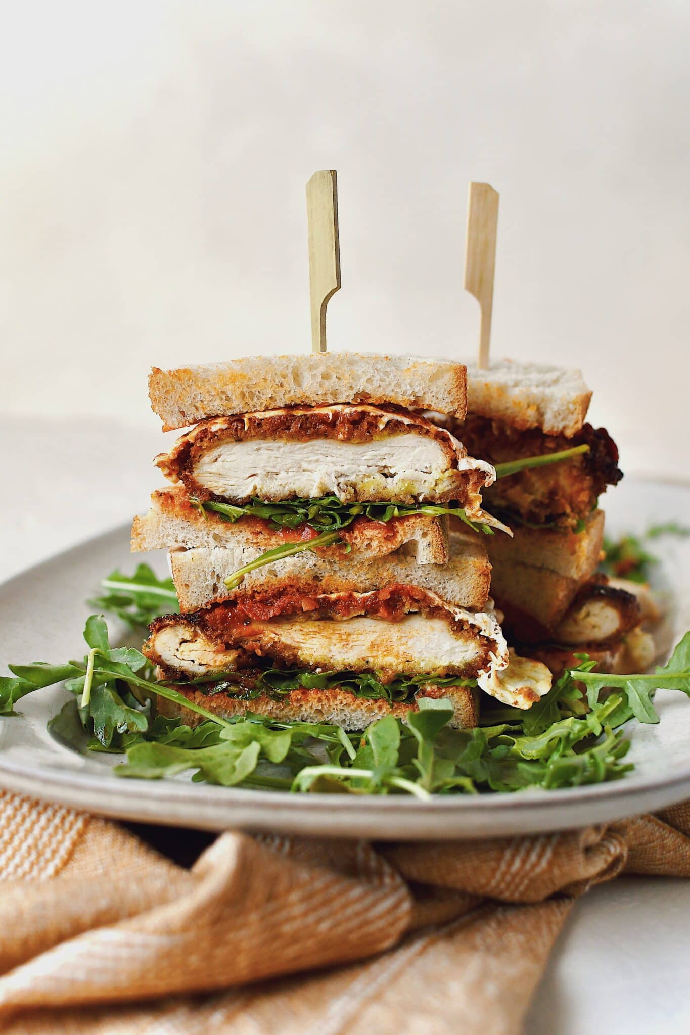 Parmesan Chicken Sandwich, sliced and stacked, on a platter on a bed of arugula.