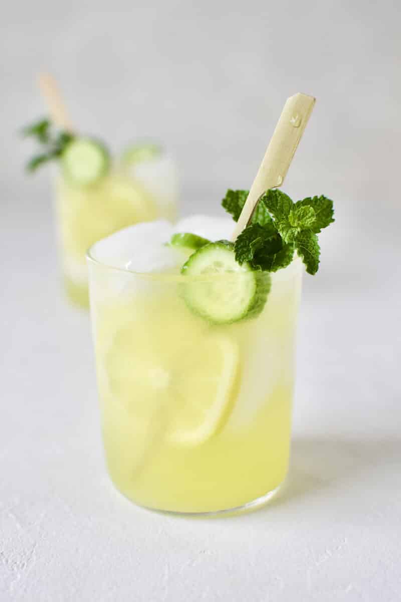 Cucumber Mint Lemonade in a glass with a skewer of lemon and cucumber slices and a sprig of mint.