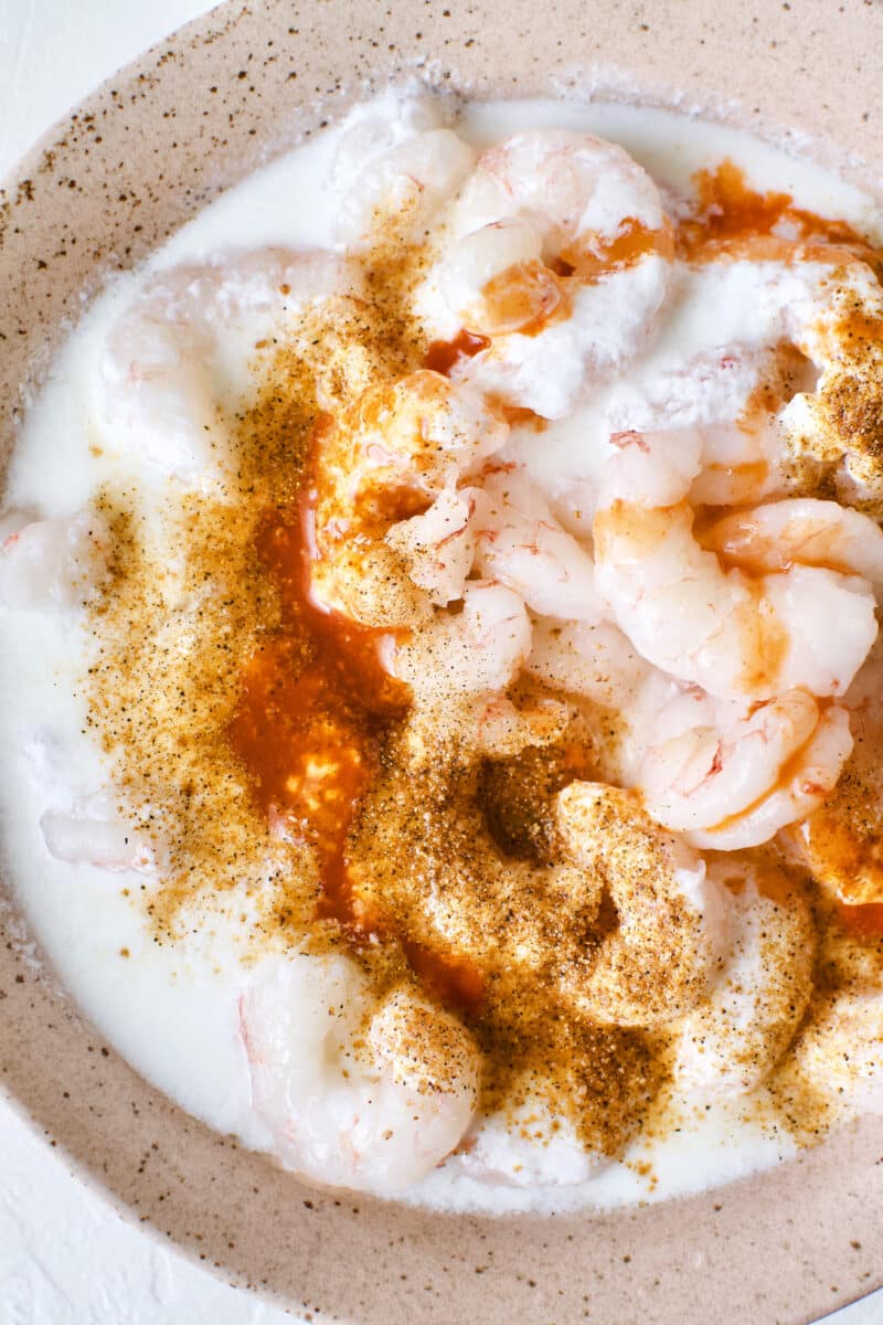 Marinating the shrimp in buttermilk, hot sauce, and creole seasoning.