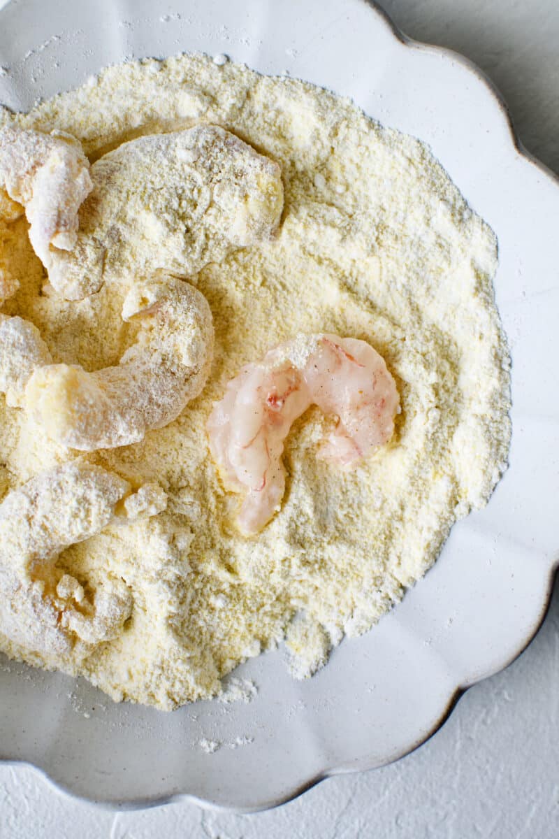 Tossing marinated shrimp in flour and cornmeal mixture to create a crispy coating.