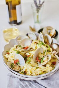 Linguine with Clam Sauce served in a bowl with a glass of white wine in the background.