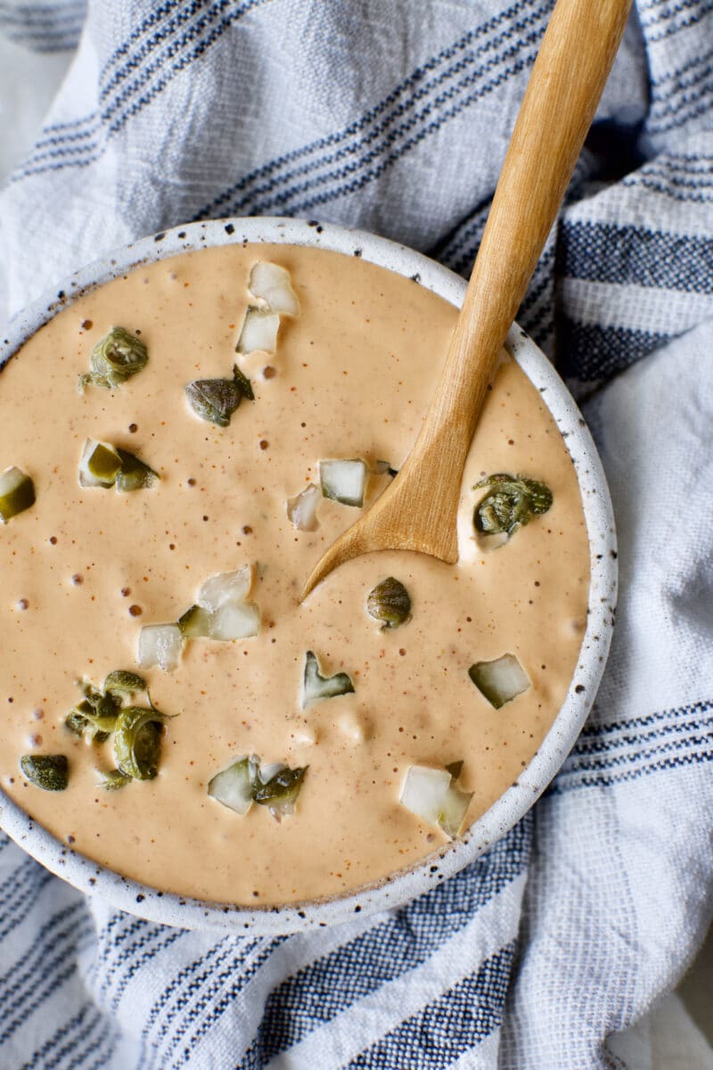 Easy Remoulade Sauce prepared and in a bowl topped with diced dill pickle pieces and caper pieces.