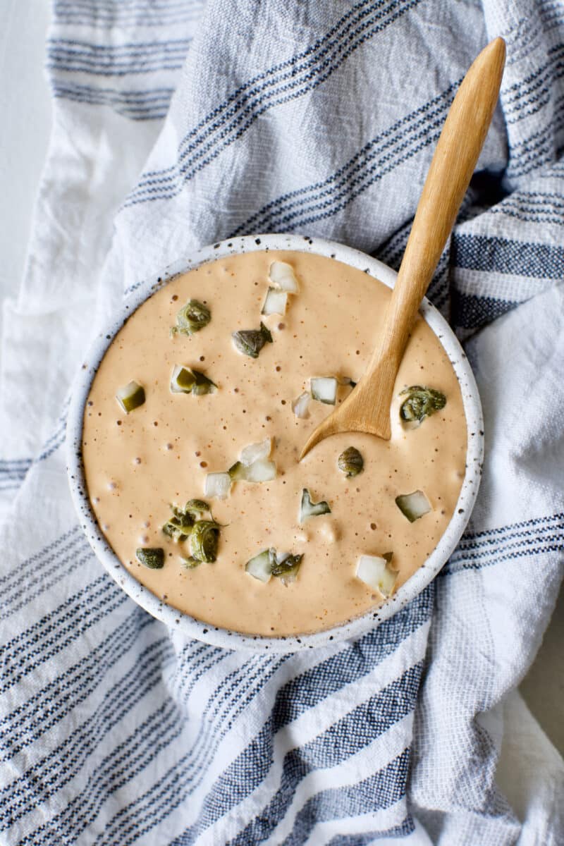 Easy Remoulade Sauce prepared and in a bowl topped with diced dill pickle pieces and caper pieces.