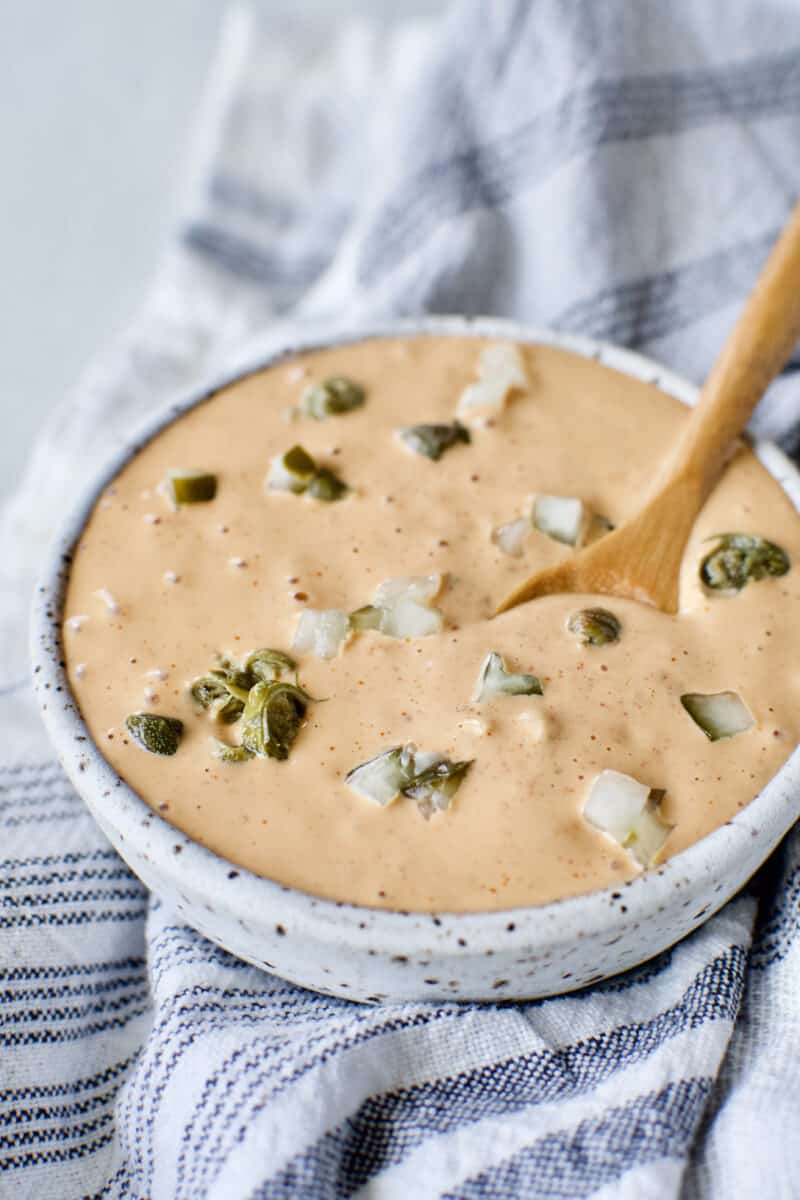 Easy Remoulade Sauce prepared and in a bowl topped with diced dill pickle pieces and caper pieces.