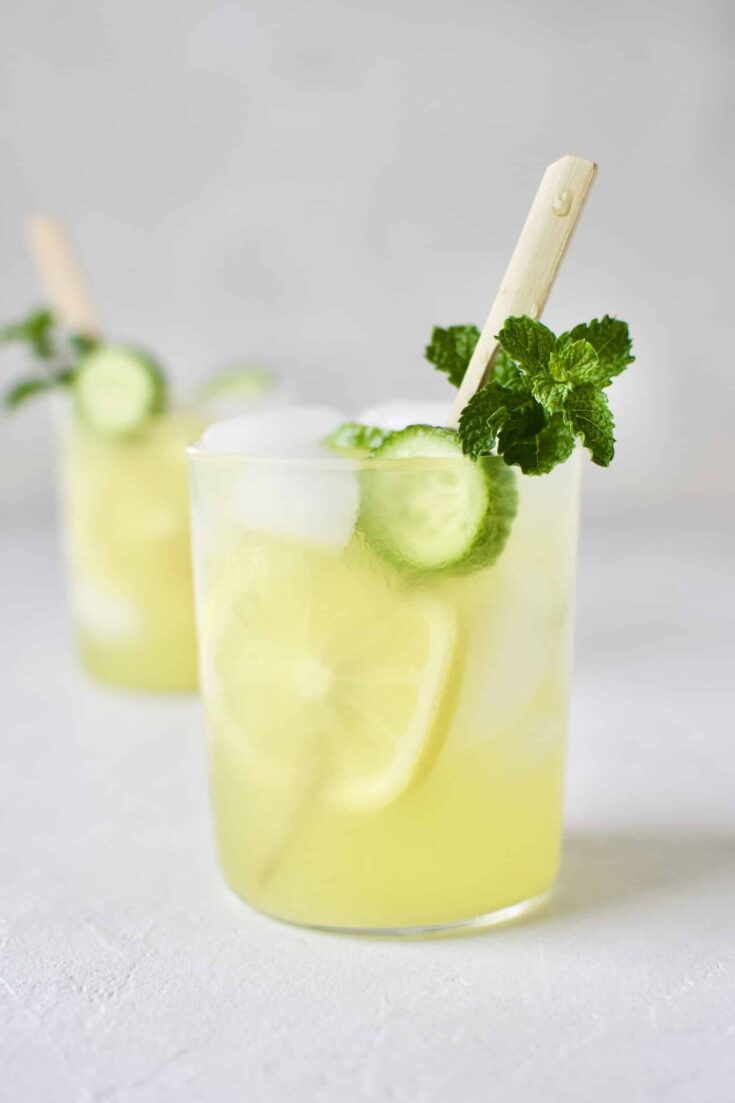 Cucumber Mint Lemonade in a glass with a skewer of lemon and cucumber slices and a sprig of mint.