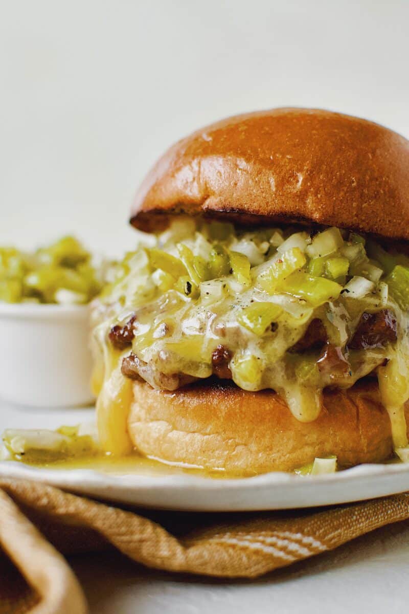 Finished Green Chili Cheeseburger, on a brioche bun, topped with hatch salsa, and cheese melting down the side.