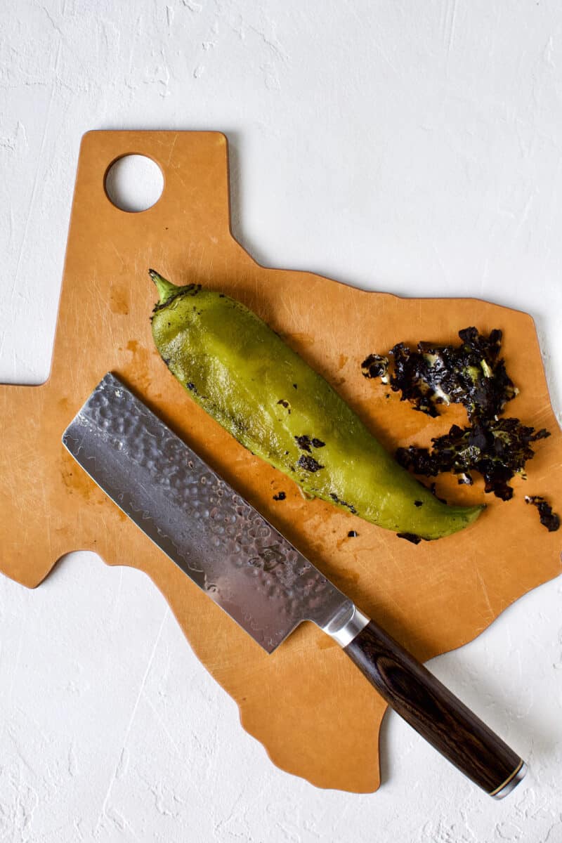 Cleaning a hatch chile by removing the charred skin with the back of a knife.