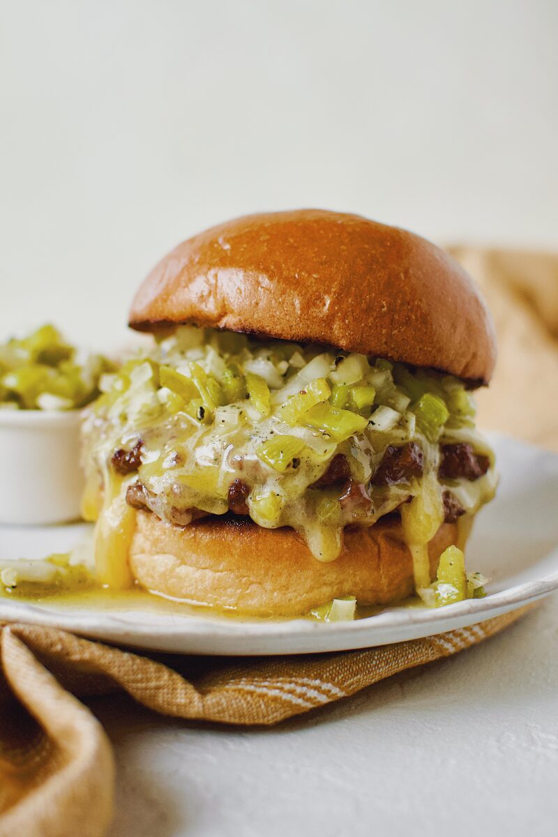 Finished Green Chili Cheeseburger, on a brioche bun, topped with hatch salsa, and cheese melting down the side.