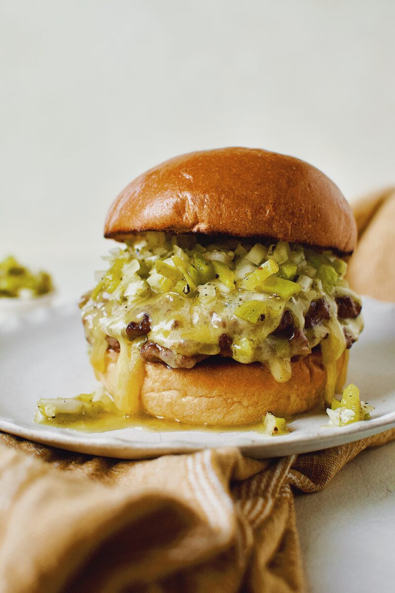 Finished Green Chili Cheeseburger, on a brioche bun, topped with hatch salsa, and cheese melting down the side.