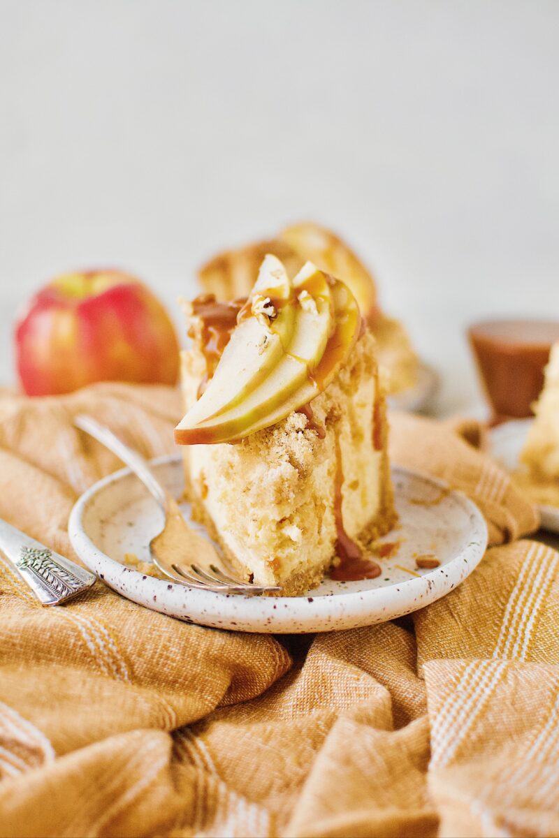 Caramel Apple Crisp Cheesecake topped with caramel sauce and sliced apples.