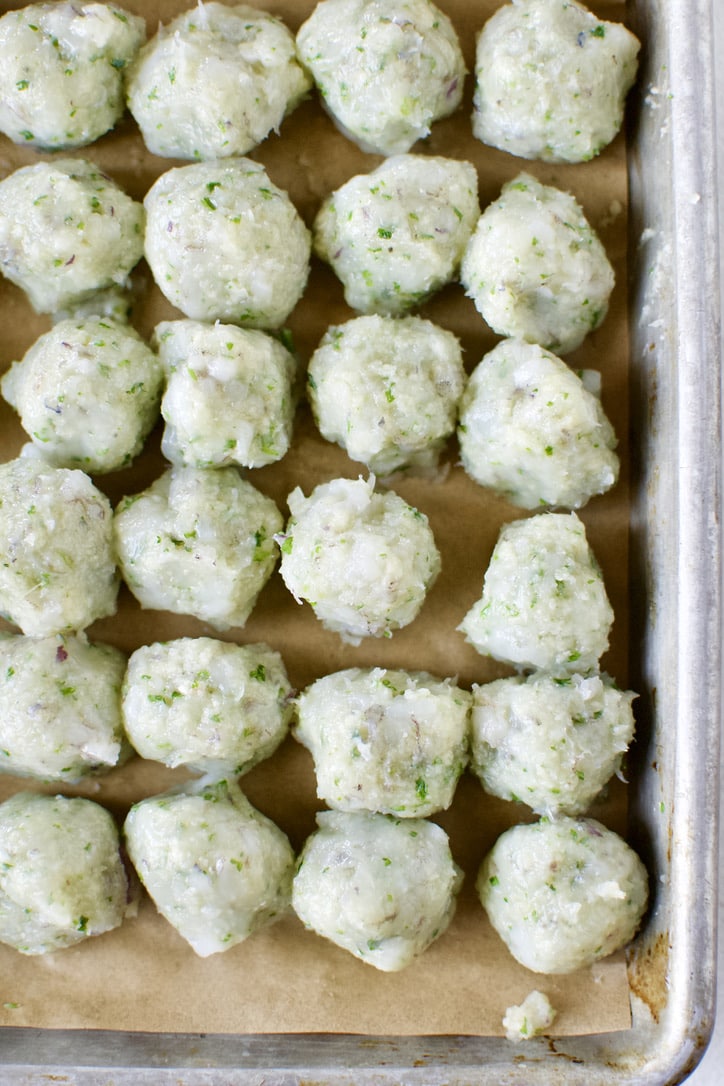 Shrimp ball mixture scooped out and portined on a sheet pan lined with parchment paper. Smoothed with wet hands.