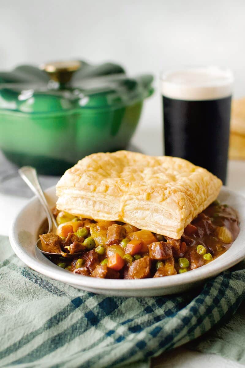 Beef Pot Pie topped with an Irish Cheddar Puff Pastry Square, ready to eat with a Guinness in the background.