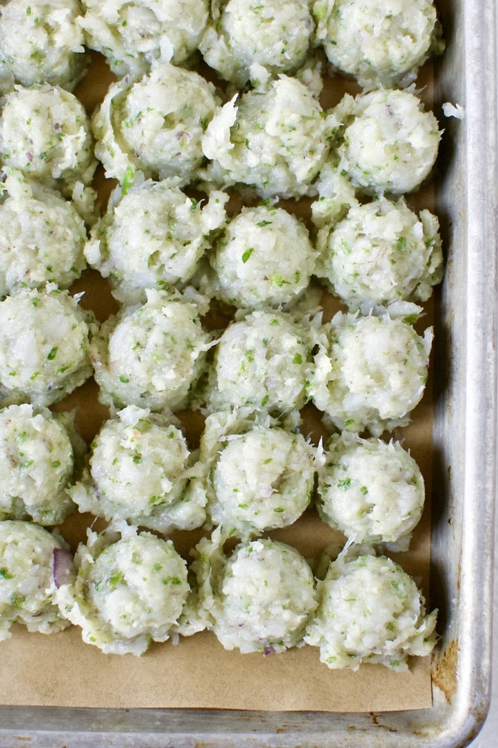 Shrimp ball mixture scooped out and portined on a sheet pan lined with parchment paper.