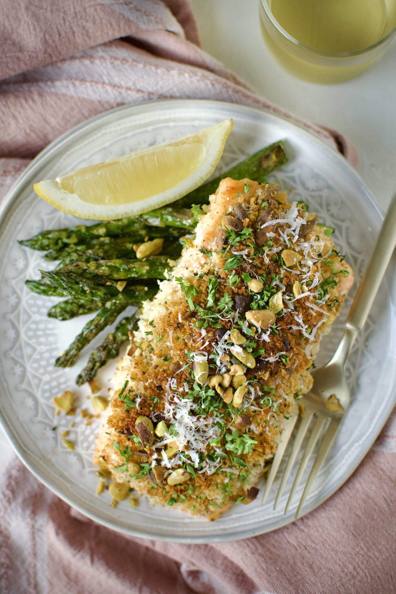 Pistachio Crusted Salmon on a plate with some grilled asparagus and a lemon wedge. Ready to eat.