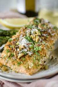 Pistachio Crusted Salmon on a plate with some grilled asparagus and a lemon wedge. Ready to eat.