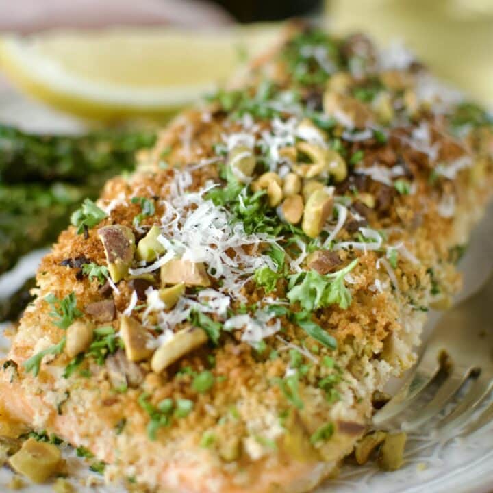 Pistachio Crusted Salmon on a plate with some grilled asparagus and a lemon wedge. Ready to eat.