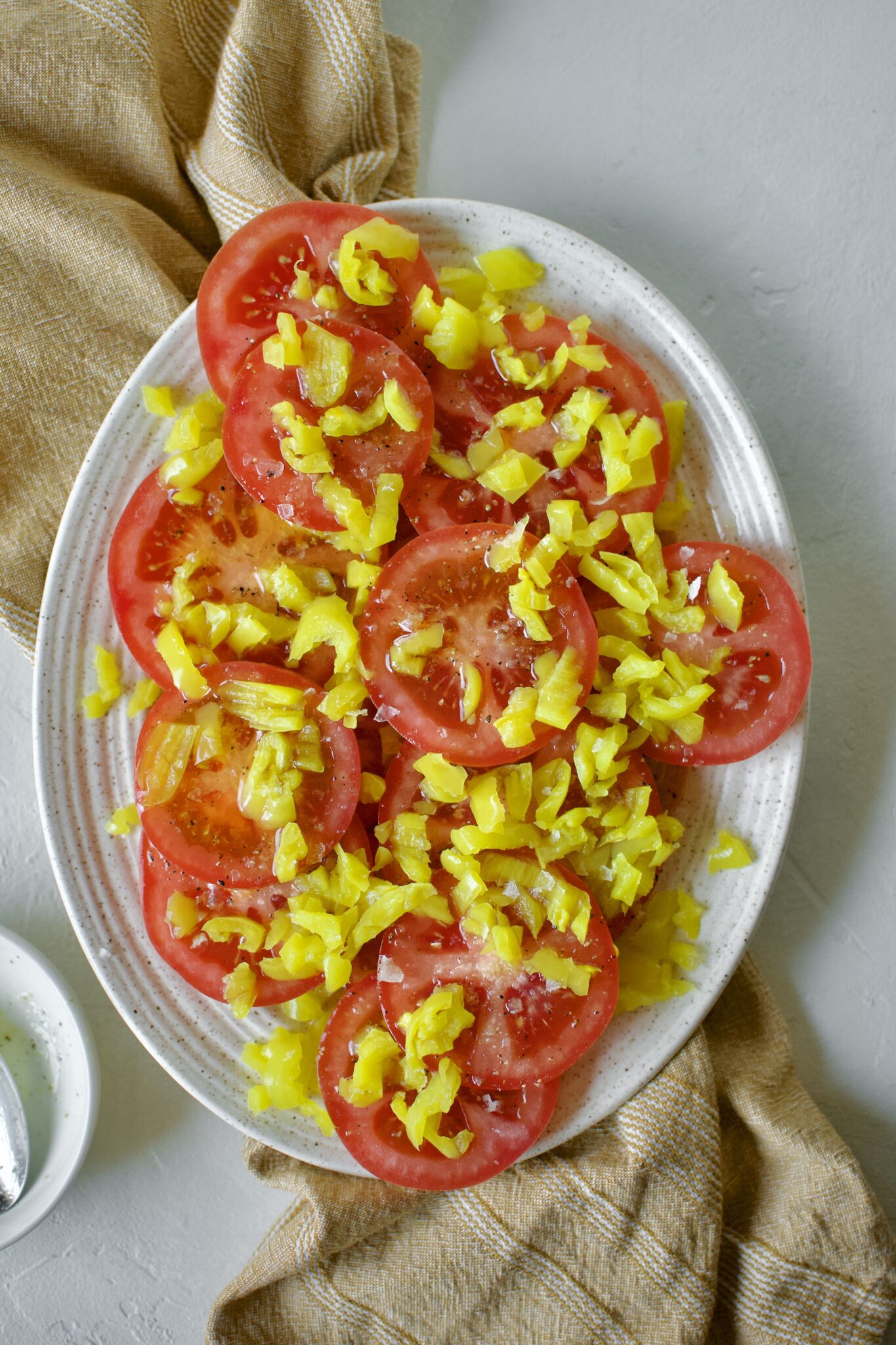 Tomato slices on a platter, topped with chopped banana pepper pieces and banana pepper vinaigrette.